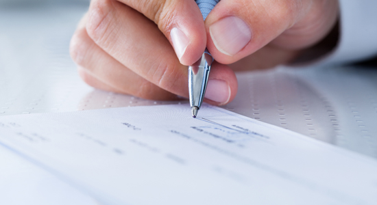 image of a hand signing a cheque