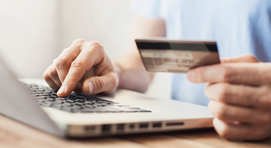 image of hand typing on laptop and holding credit card